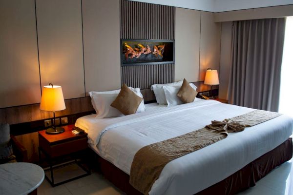 The image shows a neatly arranged hotel room with a large bed, elegant lighting, and modern decor, exuding a warm and inviting ambiance.