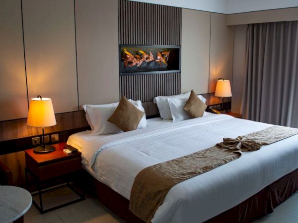 The image shows a neatly arranged hotel room with a large bed, elegant lighting, and modern decor, exuding a warm and inviting ambiance.