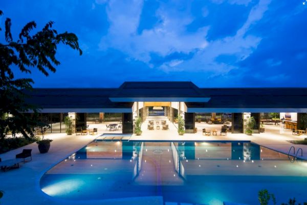 A luxurious modern building with a large illuminated pool in front, set against a twilight sky.