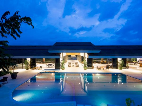 A luxurious modern building with a large illuminated pool in front, set against a twilight sky.