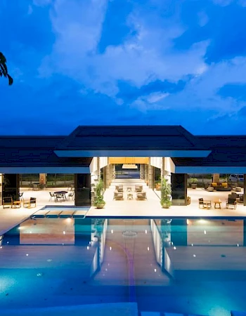 A luxurious building with a large illuminated pool and open seating areas, set against a twilight sky.