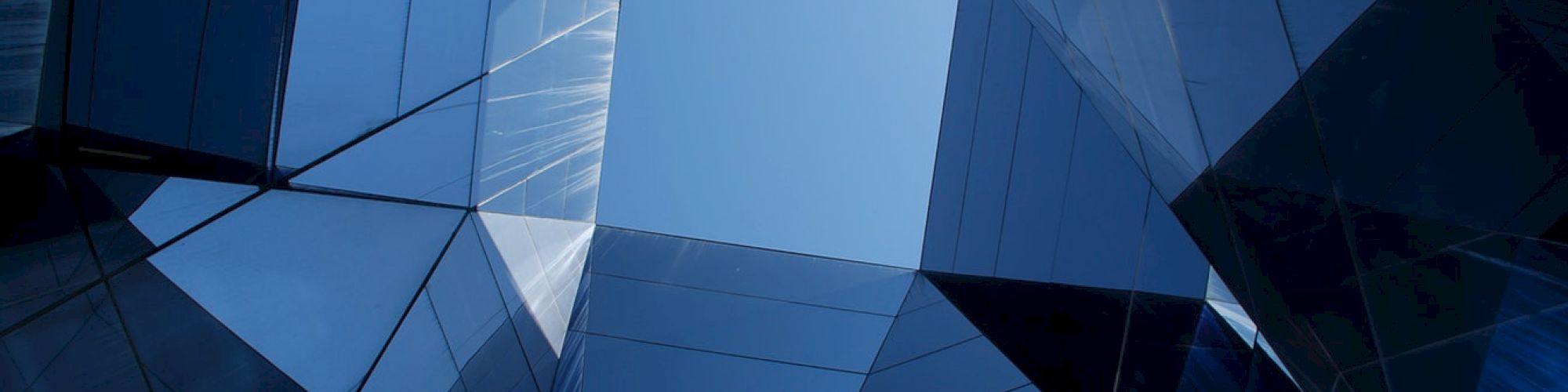 The image shows a geometric view of tall, reflective buildings creating a tunnel effect with the sky visible through the center.