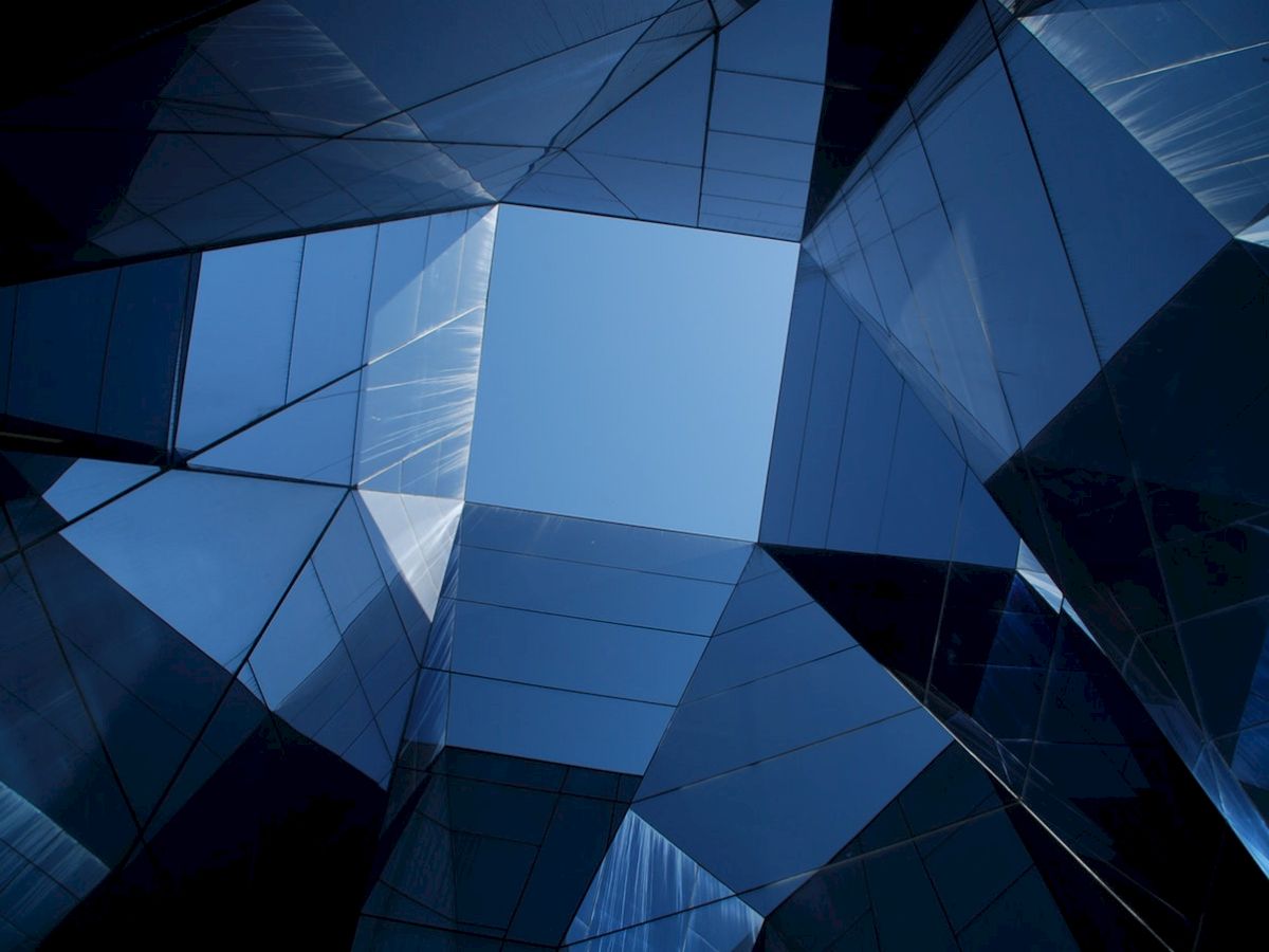 The image shows a geometric architectural design with reflective glass panels forming a symmetrical opening to the sky.