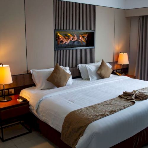 A neatly made hotel room with a large bed, two bedside lamps, decorative pillows, and a wall-mounted decoration above the bed.