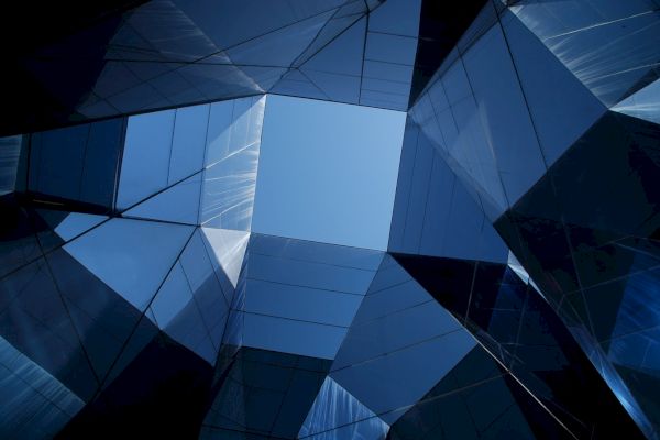 The image shows a modern architectural design with mirrored glass panels forming geometric shapes and reflecting the sky above.