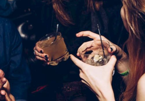 People are enjoying drinks at a social gathering, laughing and interacting with each other, creating a lively and joyful atmosphere.
