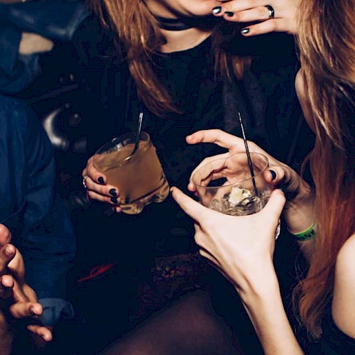 People are enjoying drinks at a social gathering, laughing and interacting with each other, creating a lively and joyful atmosphere.