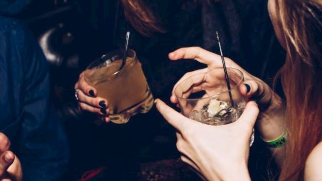 People are enjoying drinks at a social gathering, laughing and interacting with each other, creating a lively and joyful atmosphere.
