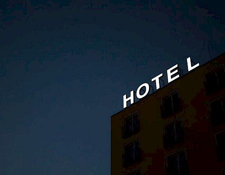 A dimly lit building with a bright "HOTEL" sign against a dark sky, missing the letter 'H'.