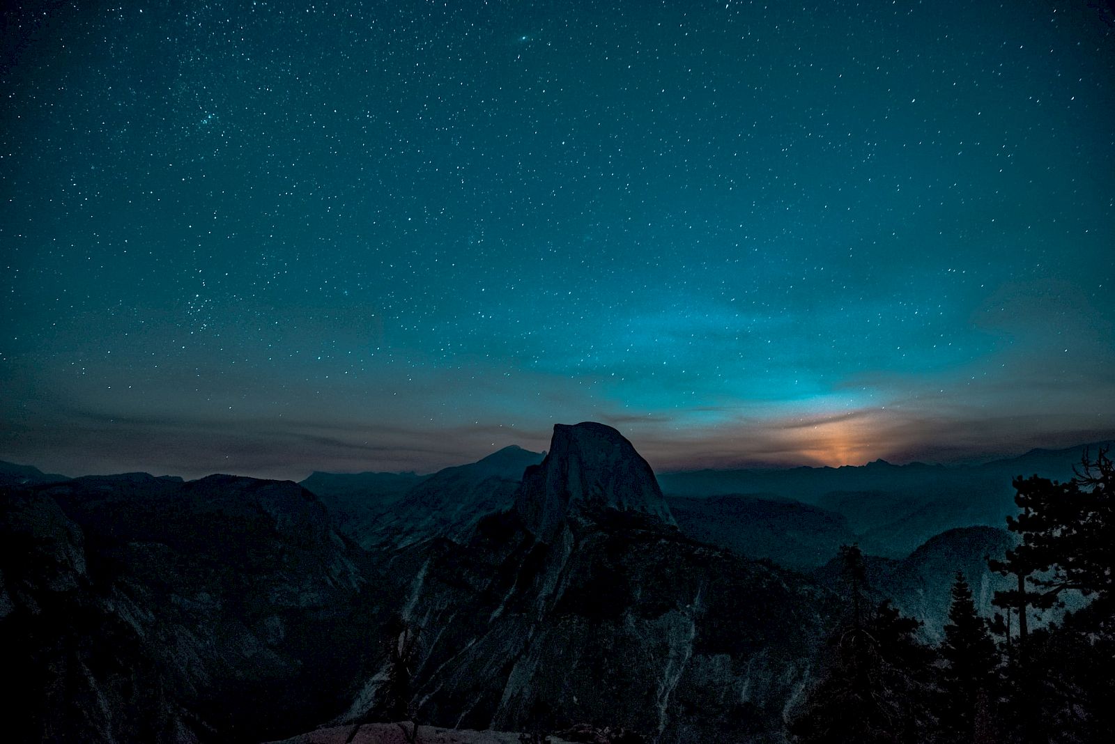 A starry night sky over a silhouetted mountain landscape with a distant glowing horizon.