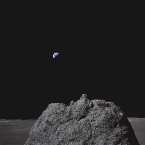 A rocky lunar surface with Earth visible in the distant dark sky.