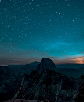 A starry night sky over a mountainous landscape with a glowing moon in the distance, creating a serene and majestic view.