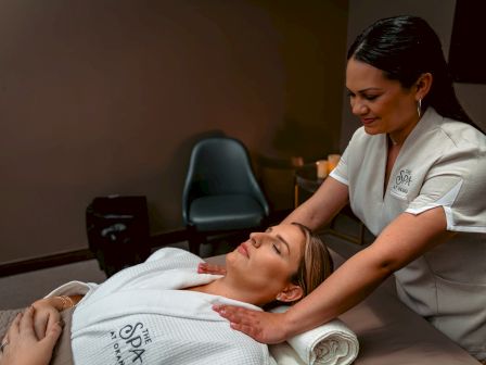 A woman is receiving a massage in a spa, lying on a table with a towel under her head. The spa therapist applies pressure gently.
