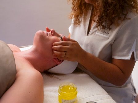 A person is receiving a facial massage from a therapist with a jar of yellow gel nearby.