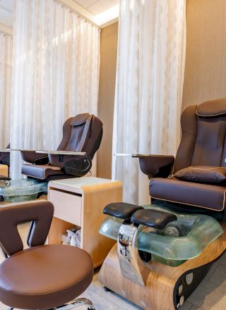 The image shows a spa or salon area with two pedicure chairs and foot baths, brown seating, and privacy curtains for clients.
