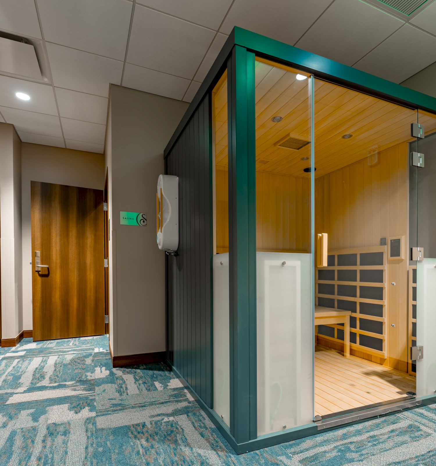 This image shows a modern sauna room with glass doors in a hallway with blue carpet and wooden accents.