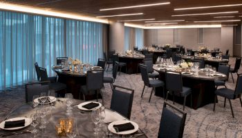 The image shows a sophisticated dining area set up for an event, with round tables, elegant place settings, and ambient lighting.