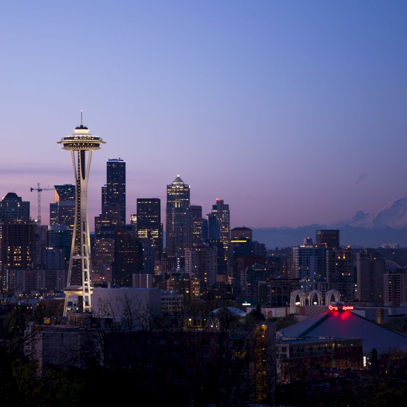 The image shows the Seattle skyline at dusk, featuring the Space Needle and city buildings, with Mount Rainier in the background.