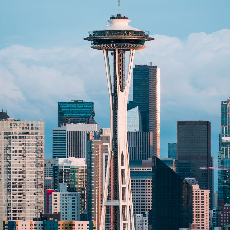 The image shows the Seattle skyline with the Space Needle prominently in the foreground, surrounded by modern skyscrapers and a cloudy sky.