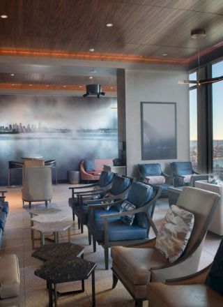 A modern lounge with comfortable seating, large windows providing a scenic view, and a cityscape artwork on the wall.