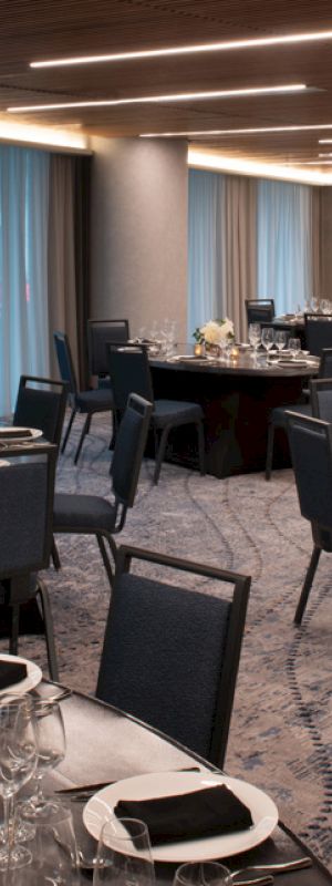 The image shows a banquet hall with round tables set for an event, featuring elegant decor and dim lighting.
