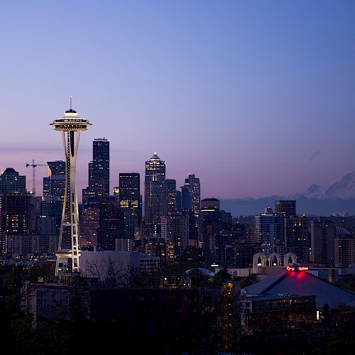 The image features the Seattle skyline at dusk, with the Space Needle prominently visible and Mount Rainier in the background.