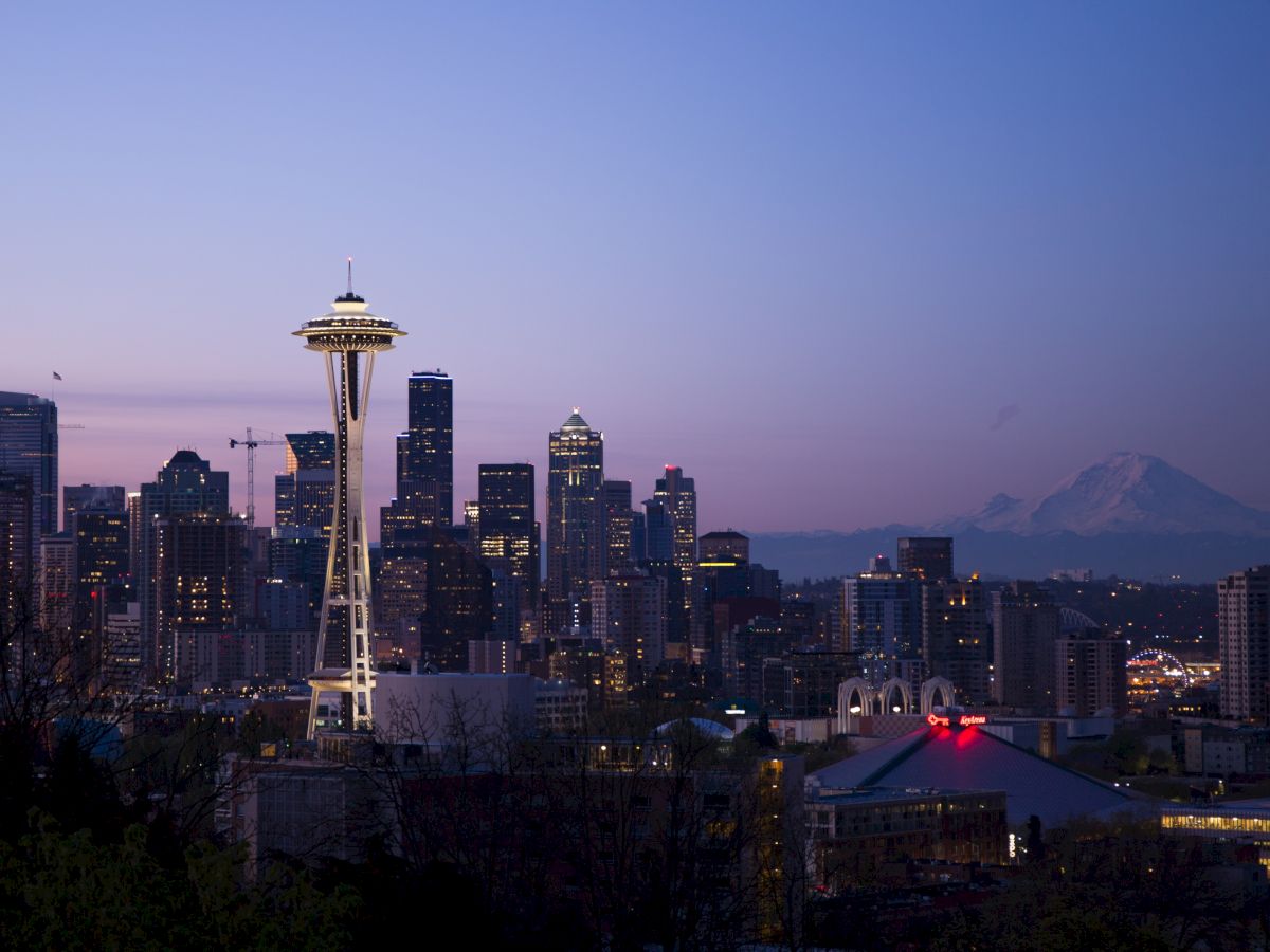 Seattle skyline at dusk with the Space Needle, skyscrapers, and Mount Rainier in the background, under a clear evening sky.