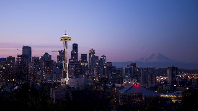 Seattle skyline at dusk with the Space Needle, skyscrapers, and Mount Rainier in the background, under a clear evening sky.