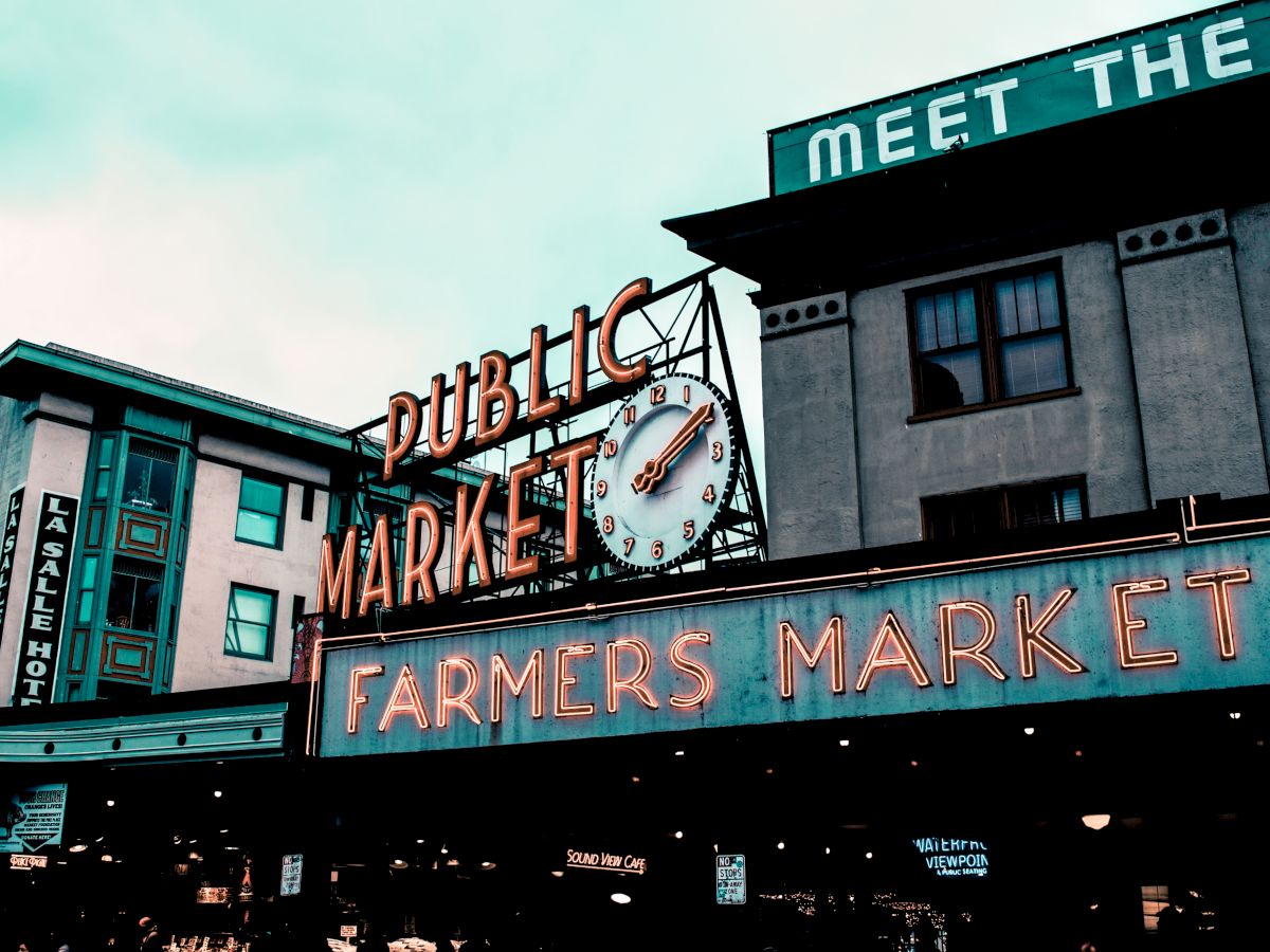 A neon sign reads "Public Market" and "Farmers Market" with a clock above, along with surrounding buildings and signage.