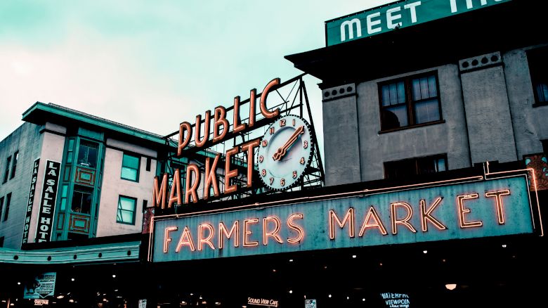 A neon sign reads "Public Market" and "Farmers Market" with a clock above, along with surrounding buildings and signage.